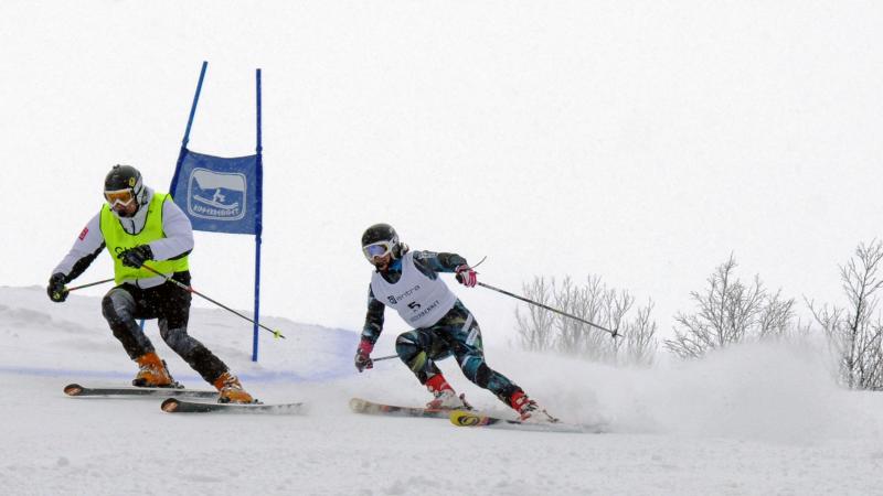 A female skier behind her guide in a Para alpine skiing competition