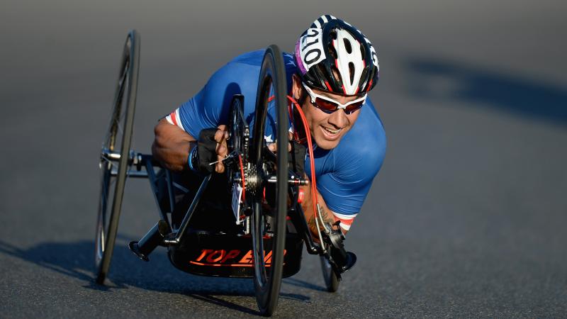 Close shot of US Para cyclist Oz Sanchez as he makes a turn on his handcycle while wearing Team USA gear