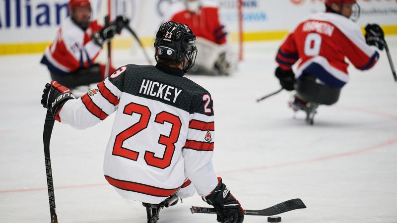 A Para ice hockey player seen from behind in a match observed by three players