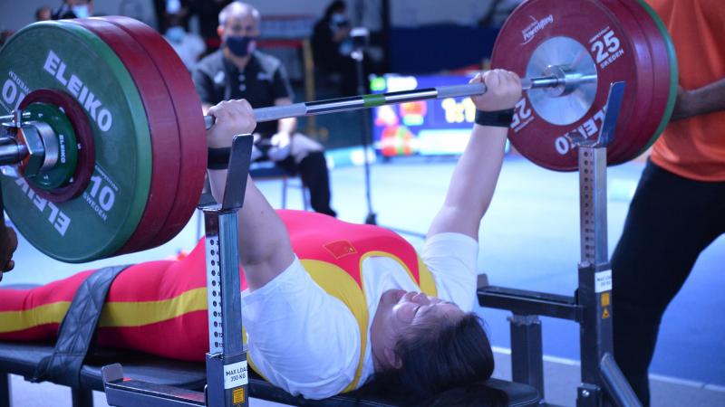 A female powerlifter making a lift observed by a group of people during a competition