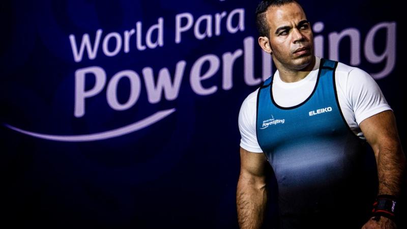 A man walking on a stage with a logo of World Para Powerlfiting in the background