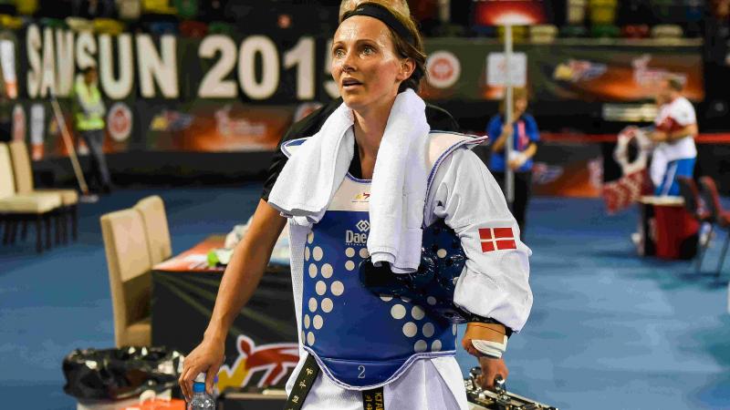 Female taekwondo athlete with right arm impairment walks off away from matt