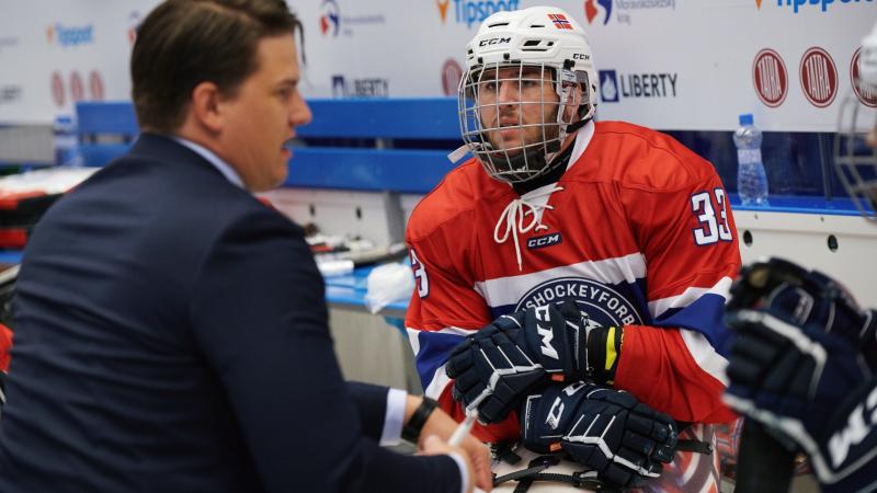 A man in a Para ice hockey uniform talking to another man in a suit in a Para ice hockey game