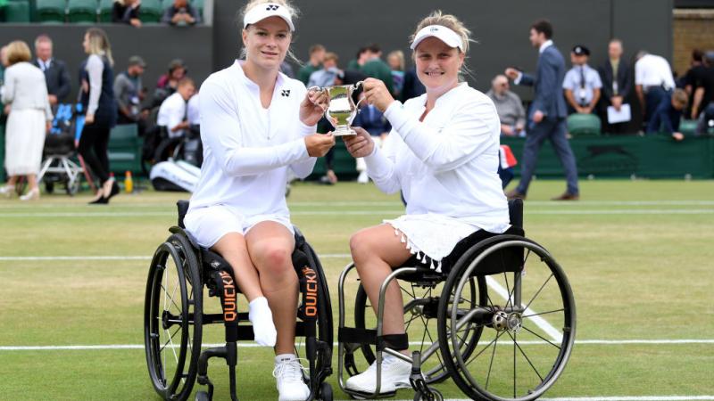 Two women in wheelchairs holding Wimbledon trophy together