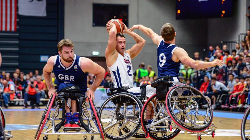 US wheelchair basketball player Jake Williams holds the ball on top of his head preventing British defenders from taking posession of it