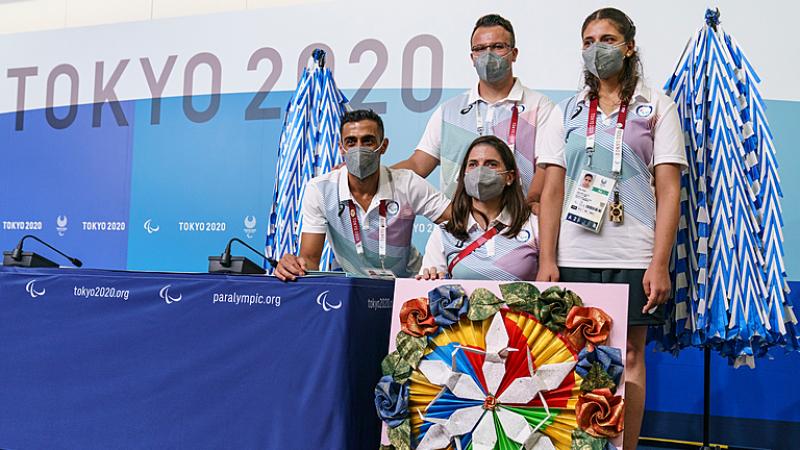 Four athletes of the Refugee Paralympic Team stand in front of a press conference background 