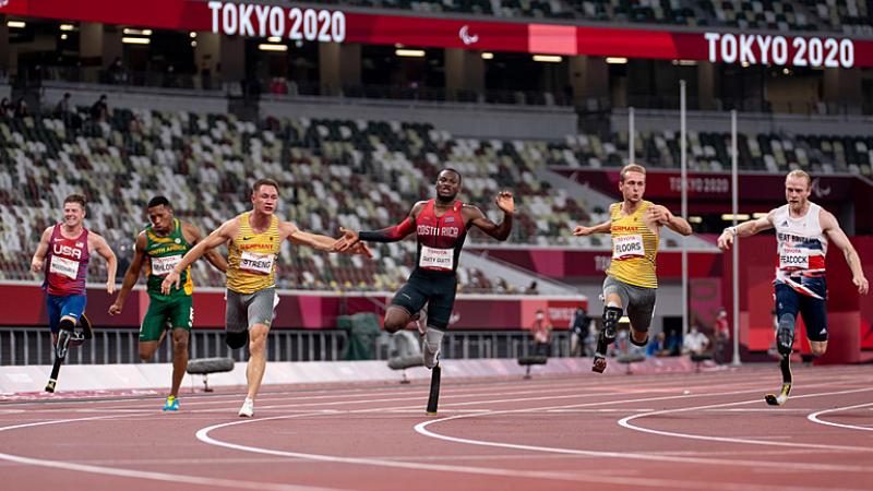 Six men with prosthetic legs crossing the line in a 100m race