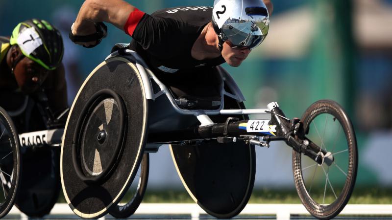 A man with a helmet pushes his wheelchair with pneumatic tyres in the Para athletics track event