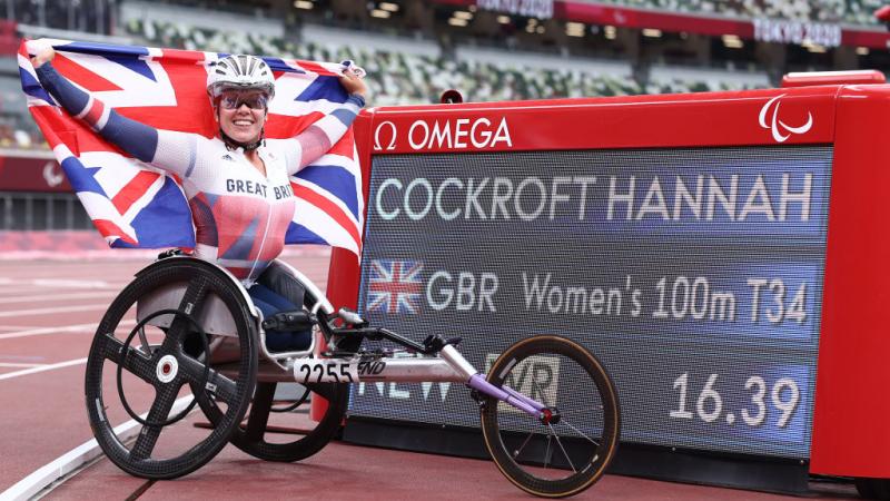 A woman in a racing wheelchair holding a British flag next to a board with her name and world record