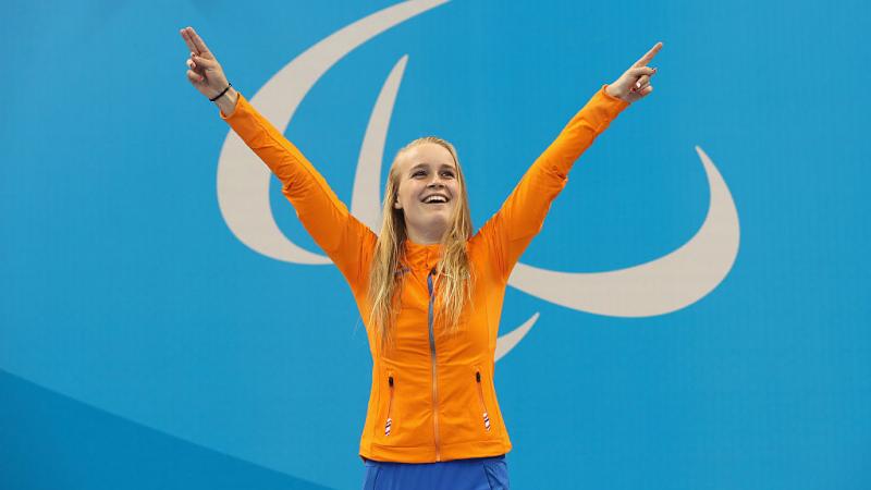 A woman with two raised hands, smiling on the podium