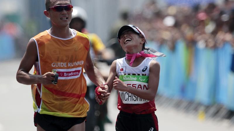 A woman running right next to a male runner guide during a marathon on a street