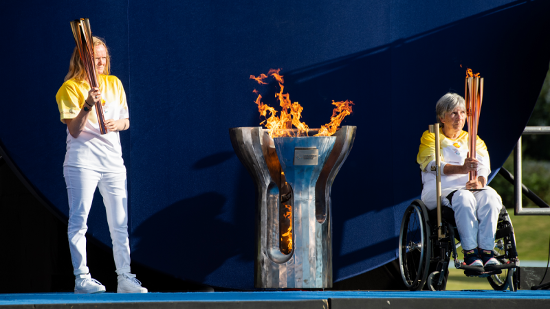 Two people holding torches with the Paralympic cauldron and flame in between
