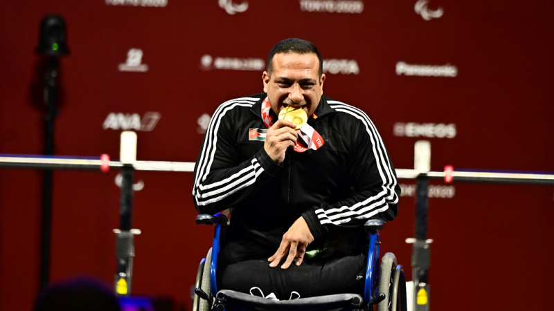 A man in a wheelchair biting his gold medal