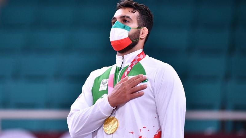 Iranian judoka Vahid Nouri with his gold medal hanging around his neck and his hand on his chest while listening to the Iranian national anthem