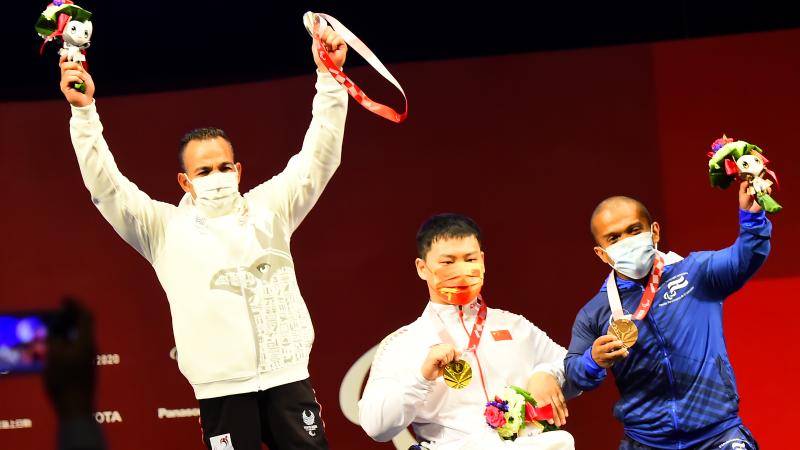 Three men showing their medals on a stage