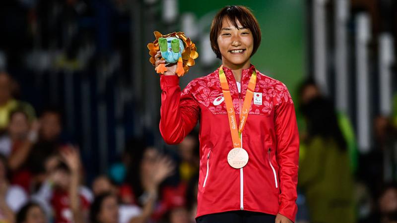 Japanese female judoka smiles on podium holding Paralympic mascot gift 