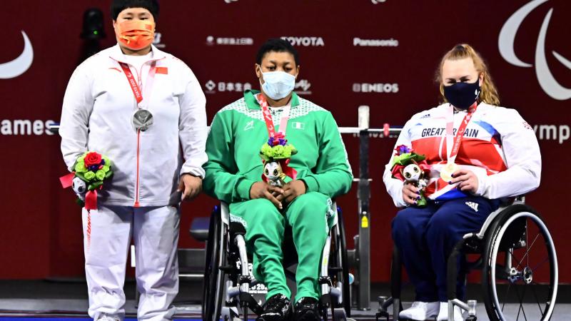 Three women posing for photos on the podium with their medals