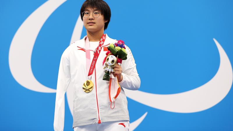 A woman poses with a gold medal, holding the mascot in her left hand