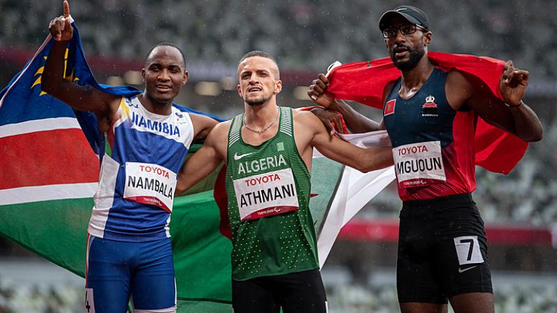 Three men on an athletics track with their flags 
