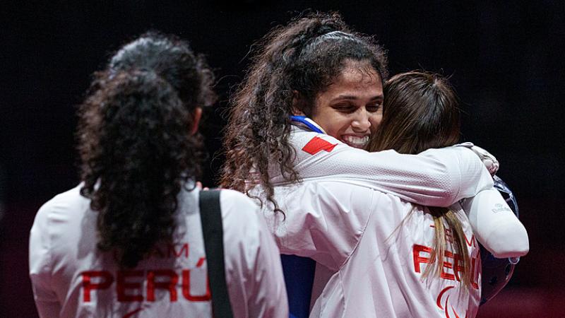 Leonor Espinoza Carranza smiles and hugs a colleague wearing a white jacker with peru on the back