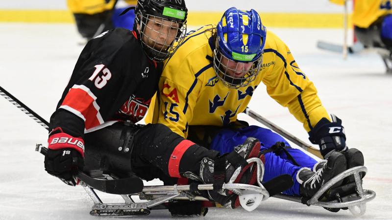 Two Para ice hockey players on sleds battling to get the puck
