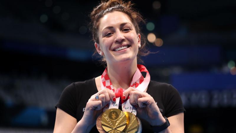 A Para swimmer posing with four medals and smiling to the camera