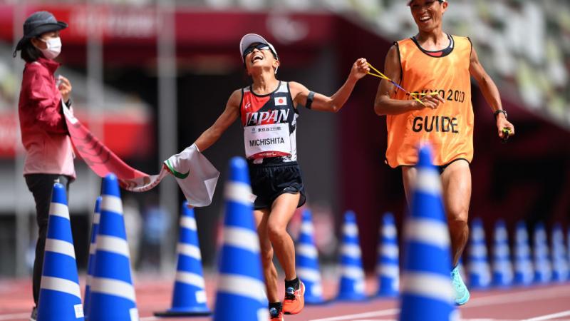 A female runner and her guide crossing the finish line in an athletics stadium