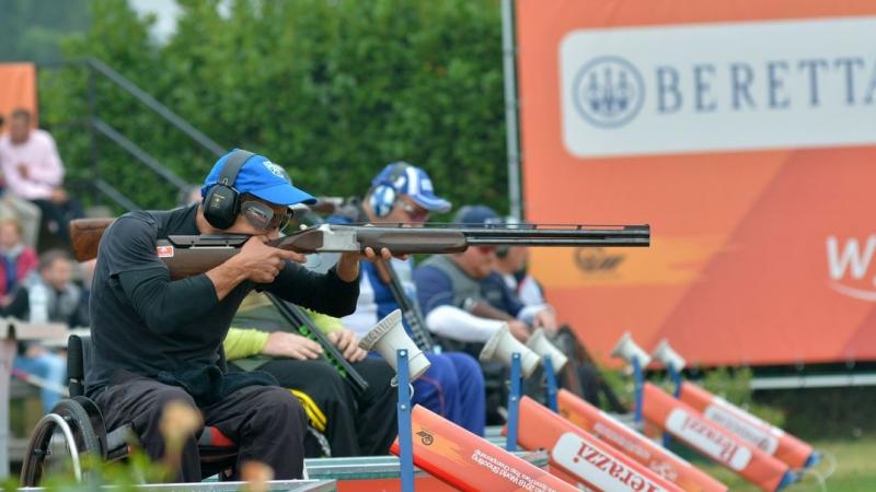 A man in a wheelchair competing with a shotgun in a Para trap event observed by other four competitors