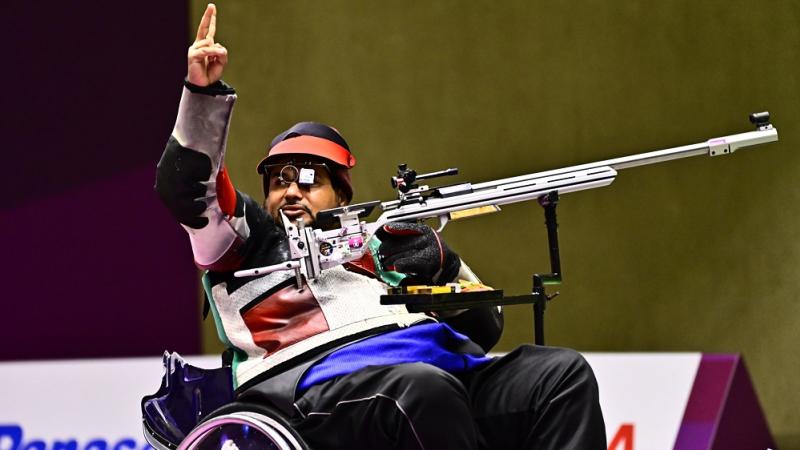 A man in a wheelchair waving in a shooting competition with a rifle