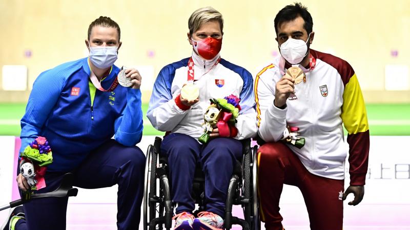 A woman and a man kneeling with their medals around a woman in a wheelchair showing her medal