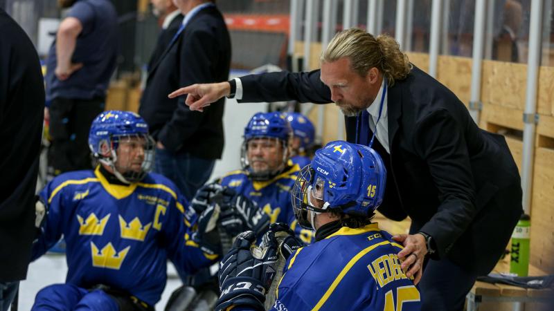 A man talking to Para ice hockey players on sleds pointing finger to the ice