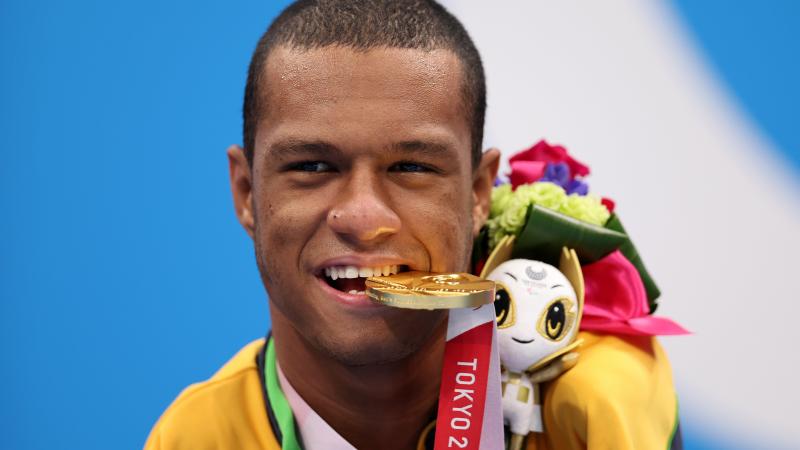 A man poses for photos biting a gold medal