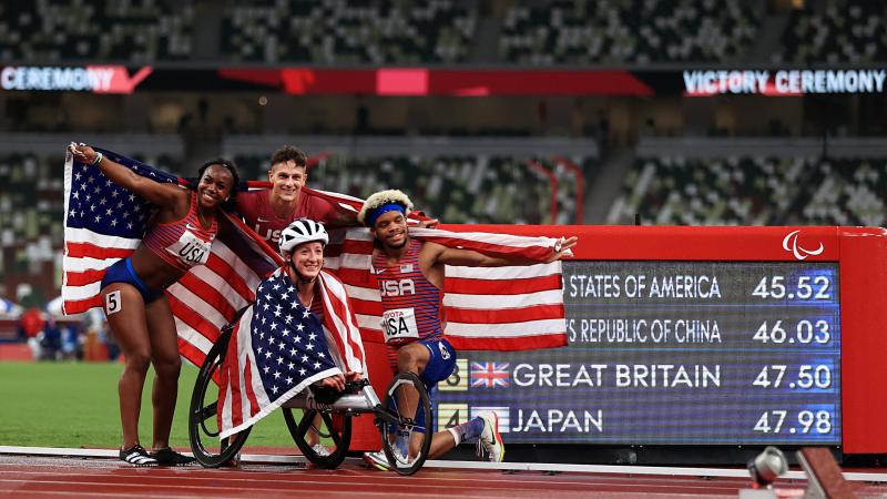 Four athletes celebrating with flags in front ofthe results screen