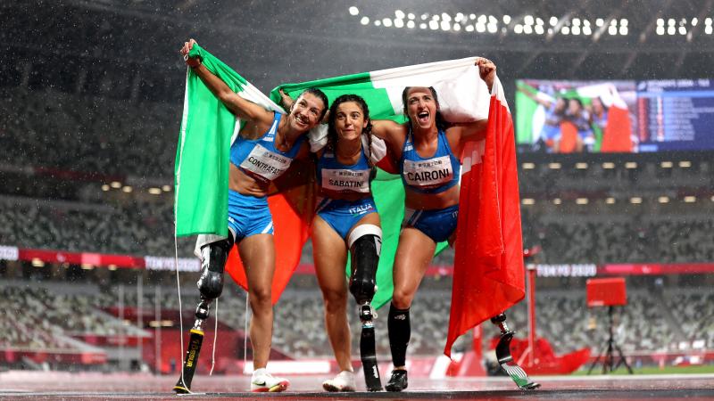 Three female athletes posing for a photo with flags while the rain is falling
