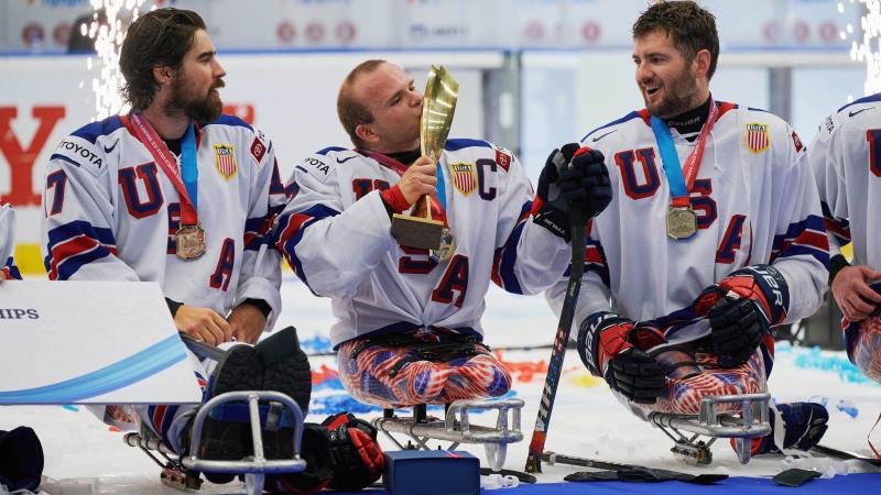 A Para ice hockey player kissing a trophy with the fireworks behind him