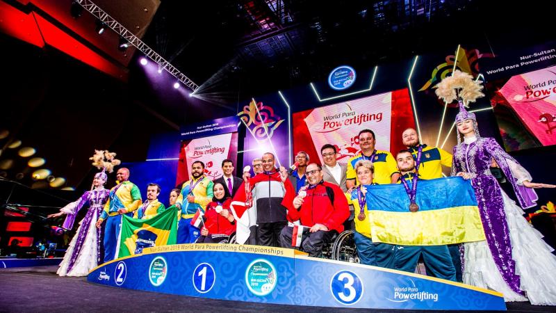 Athletes on the podium with team representatives posing for a photo with flags.