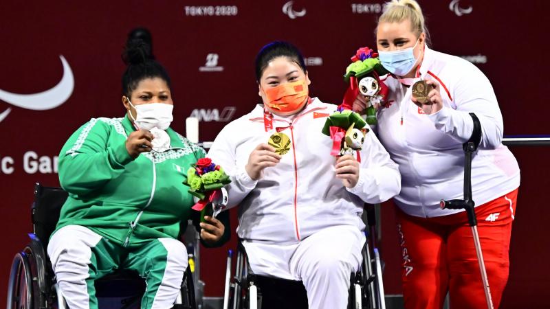 Three female athletes posing for a photo on the podium with medals around their necks.