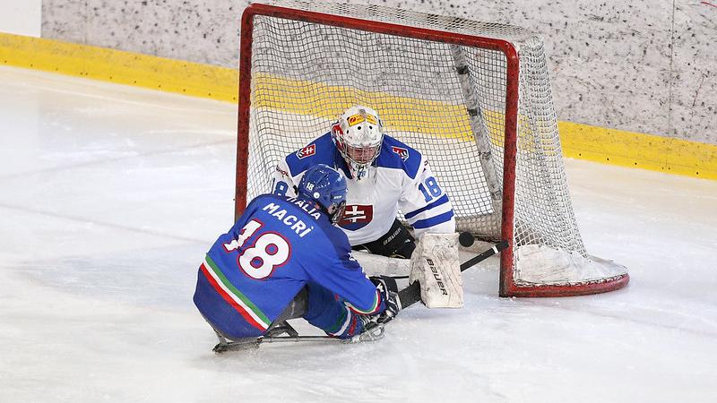 A Para ice hockey player hitting the puck in front of the goaltender