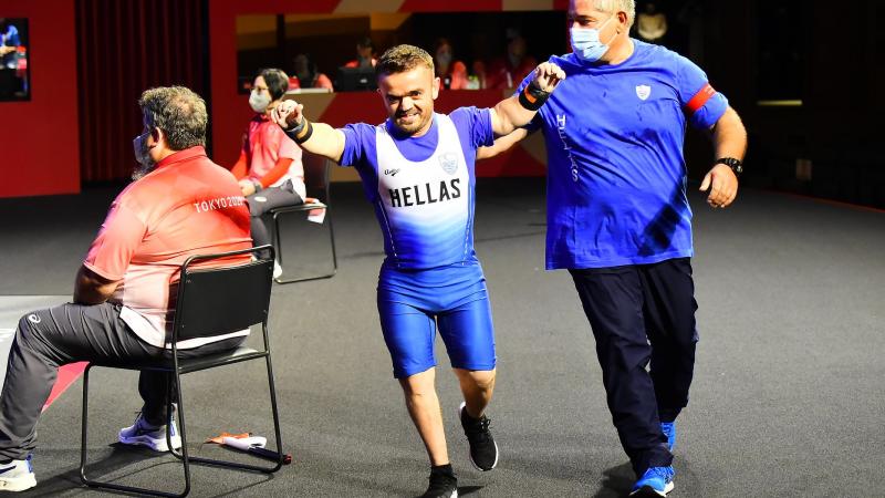 A man walking with his arms raised and a smile on his face while his coach taps him on the back.