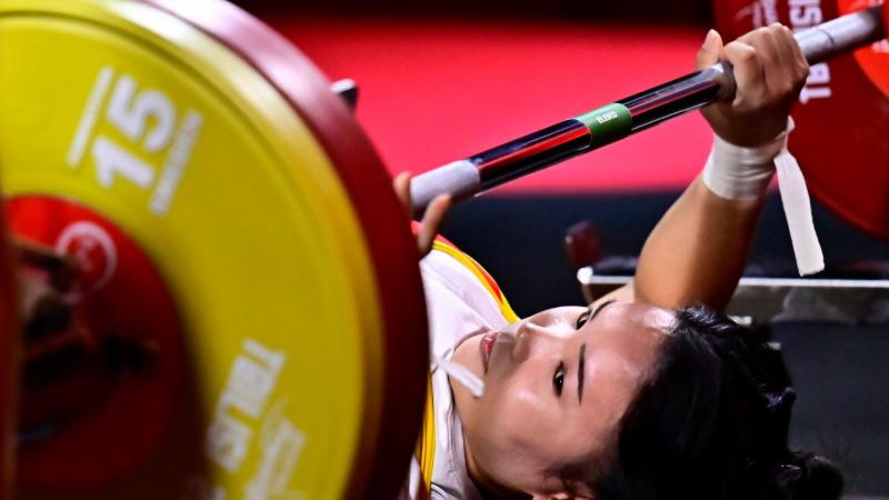 A woman on a bench press looking at the bar 