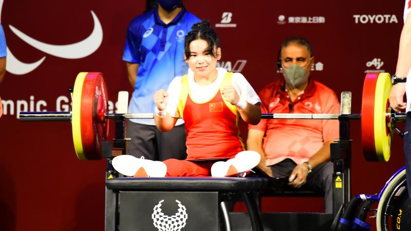 A woman sitting on a bench holding her fists high in celebration with a smile on her face