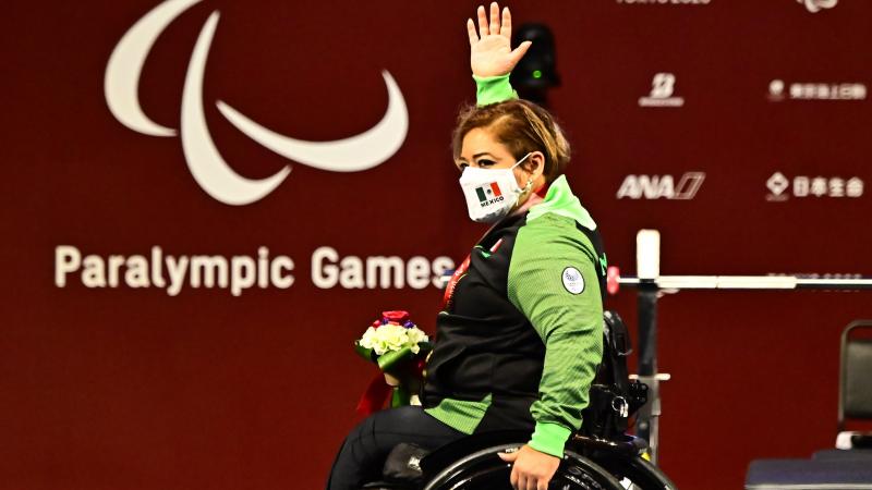 A woman in a wheelchair, raising her right hand high in celebration on the podium.