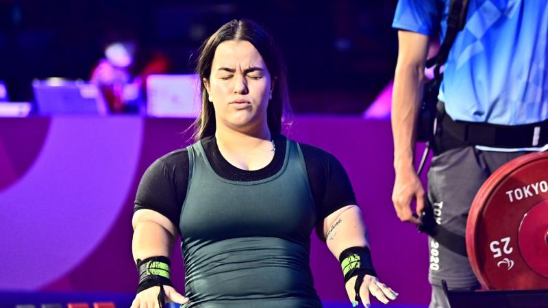 A woman standing with her eyes closed and her arms stretched with fists wide-open.