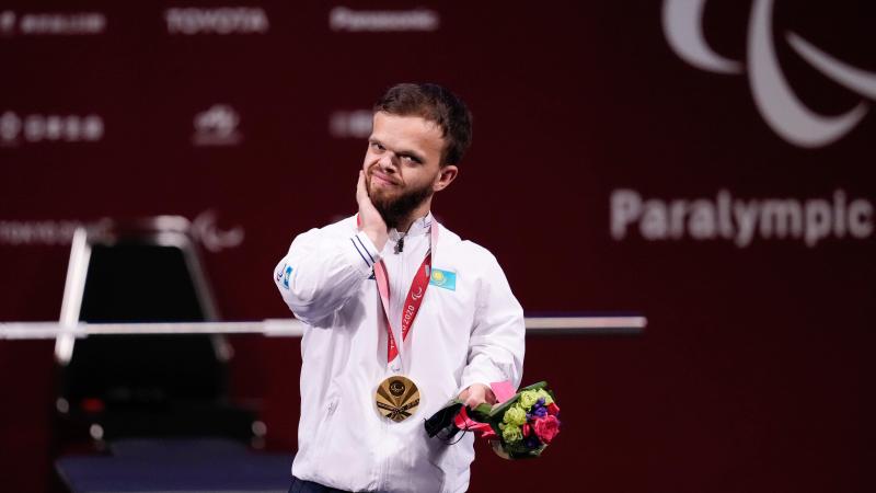 A man standing on the podium holding flowers in one hand and touching his face with the other hand