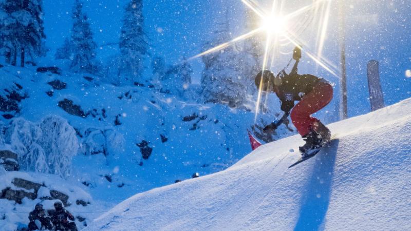 A female Para snowboarder riding on the snow with floodlights in the background