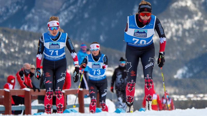 Three standing skiers climbing up the hill on a snowy road