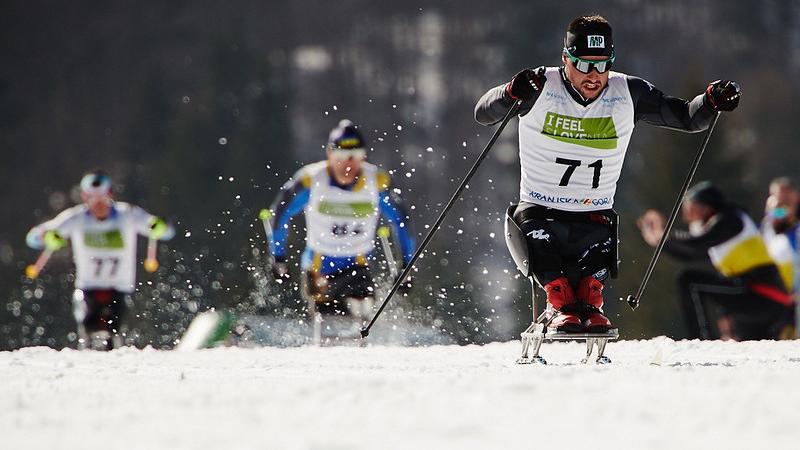 A male sit skier competing in cross-country ahead of two competitors
