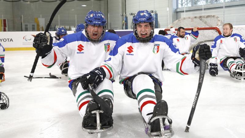 Two Italian Para ice hockey players celebrating with their team in the background in an ice rink