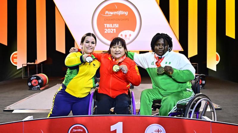 Three women on a podium showing their medals
