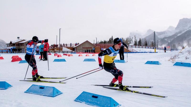 A male cross-country skier following his guide on a snowy track observed by three people